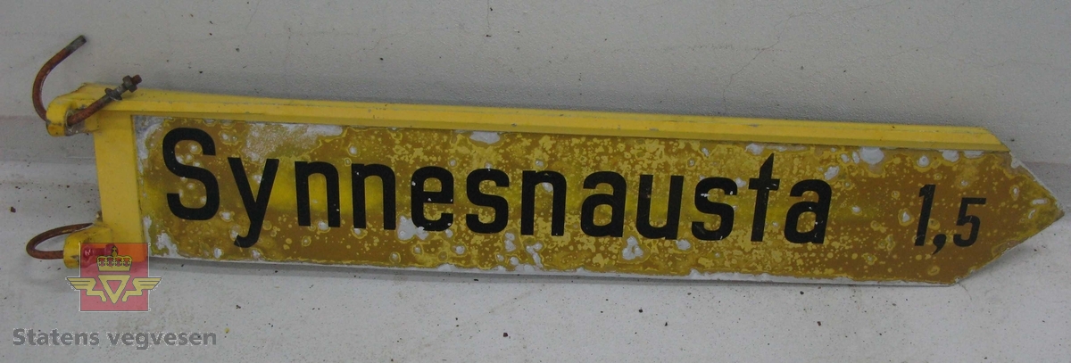Vegviserskilt. Skiltplata er lysreflekterende gul med svart tekst "Synnesnausta 1,5". Selve skiltplata er lagd av en aluminiumsplate der festet og kanten øverst er støpt i en del. Skiltet har vært festet til 3 toms stolpe ved hjelp av to bøyler som henger på skiltet.
