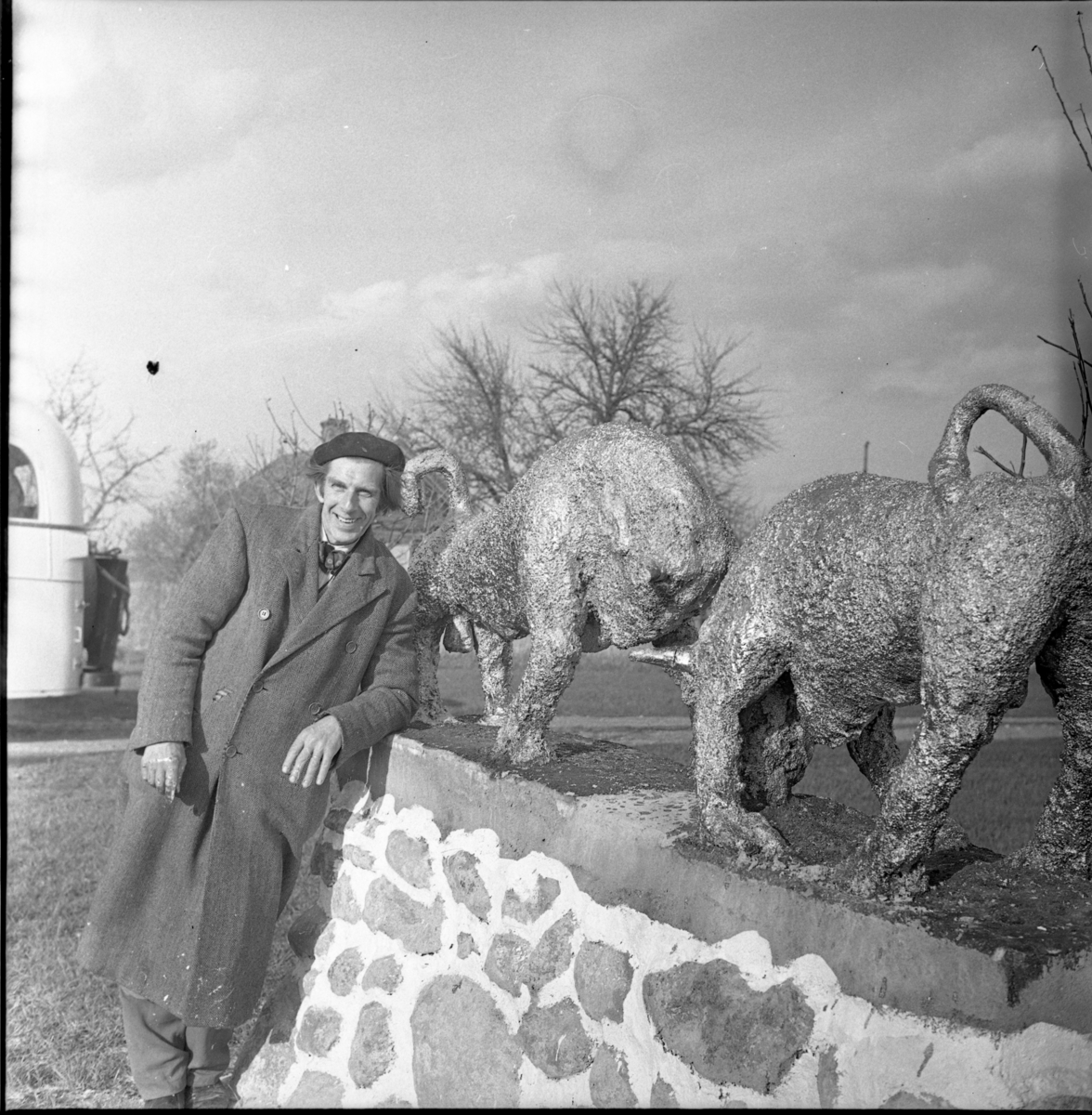 Olle Krantz i rock och med basker på huvudet lutad mot en mur med två djurskulpturer vid Tempelgården på Visingsö.