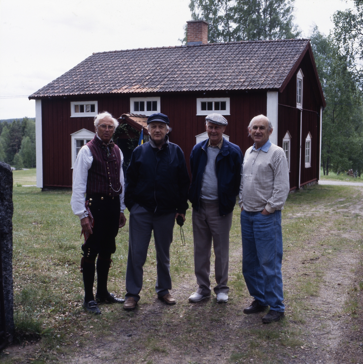 Några män, inklusive bröderna Ahnlund, står i grindhålet till ett torp, 12 juni 1994. De tittar mot fotografen. En av männen är klädd i hembygdsdräkt.
