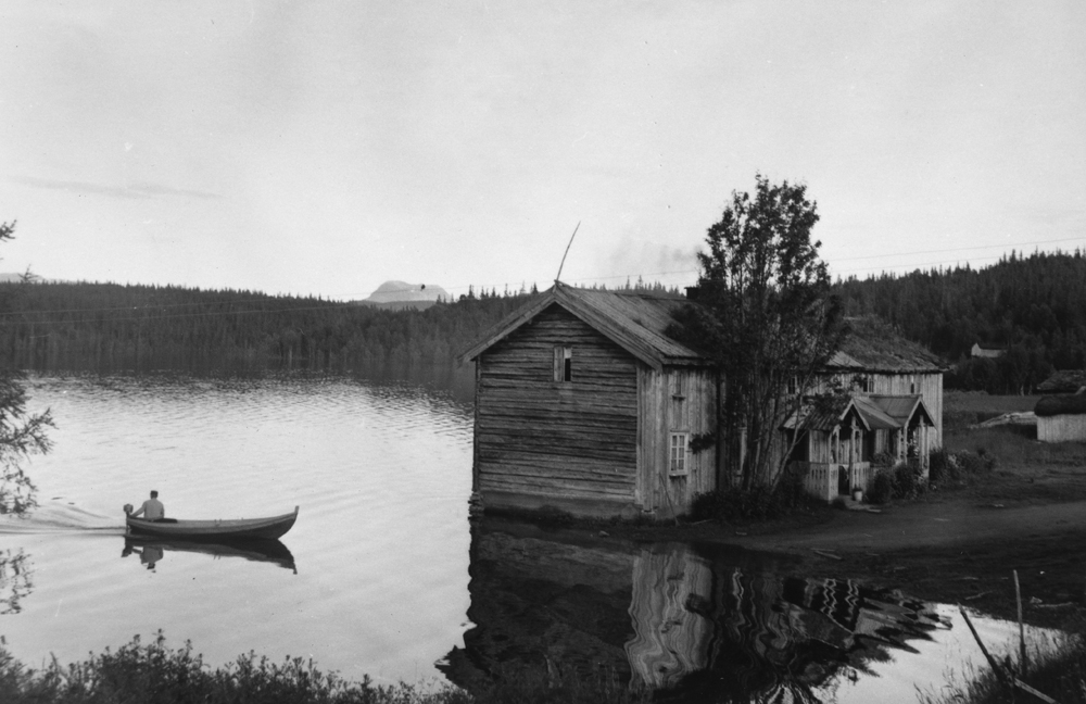 Under oppdemminga av Røssvatnet, gård i Sjåvika og mann i båt med påhengsmotor.