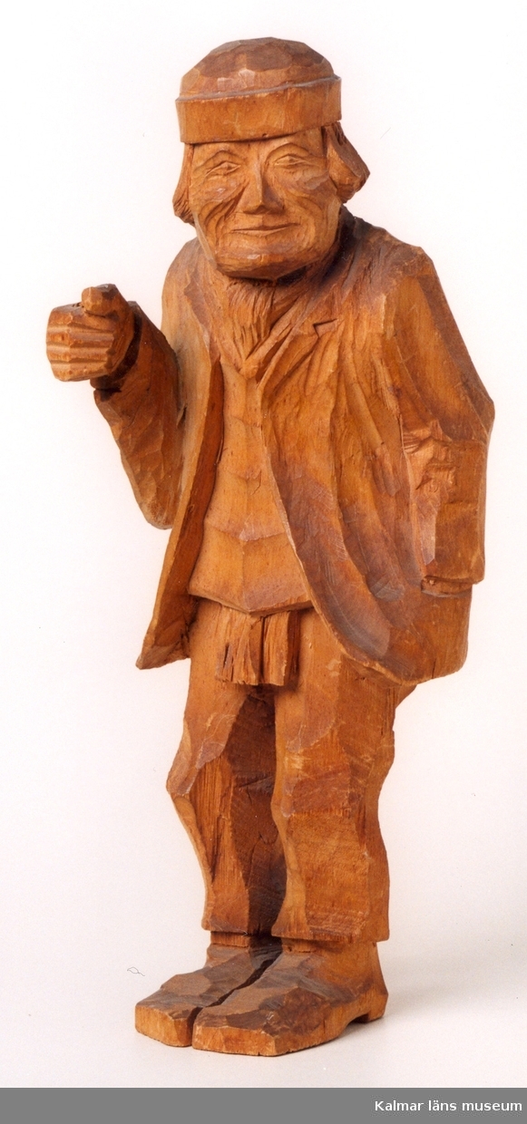 KLM 39255:8. Skulptur, av trä. Gubbe i kavaj och halsduk under tröja. På huvudet mössa utan skärm. Defekt, föremål i höger hand saknas. Signerad B. Ljunggren, Markaryd, 1919.