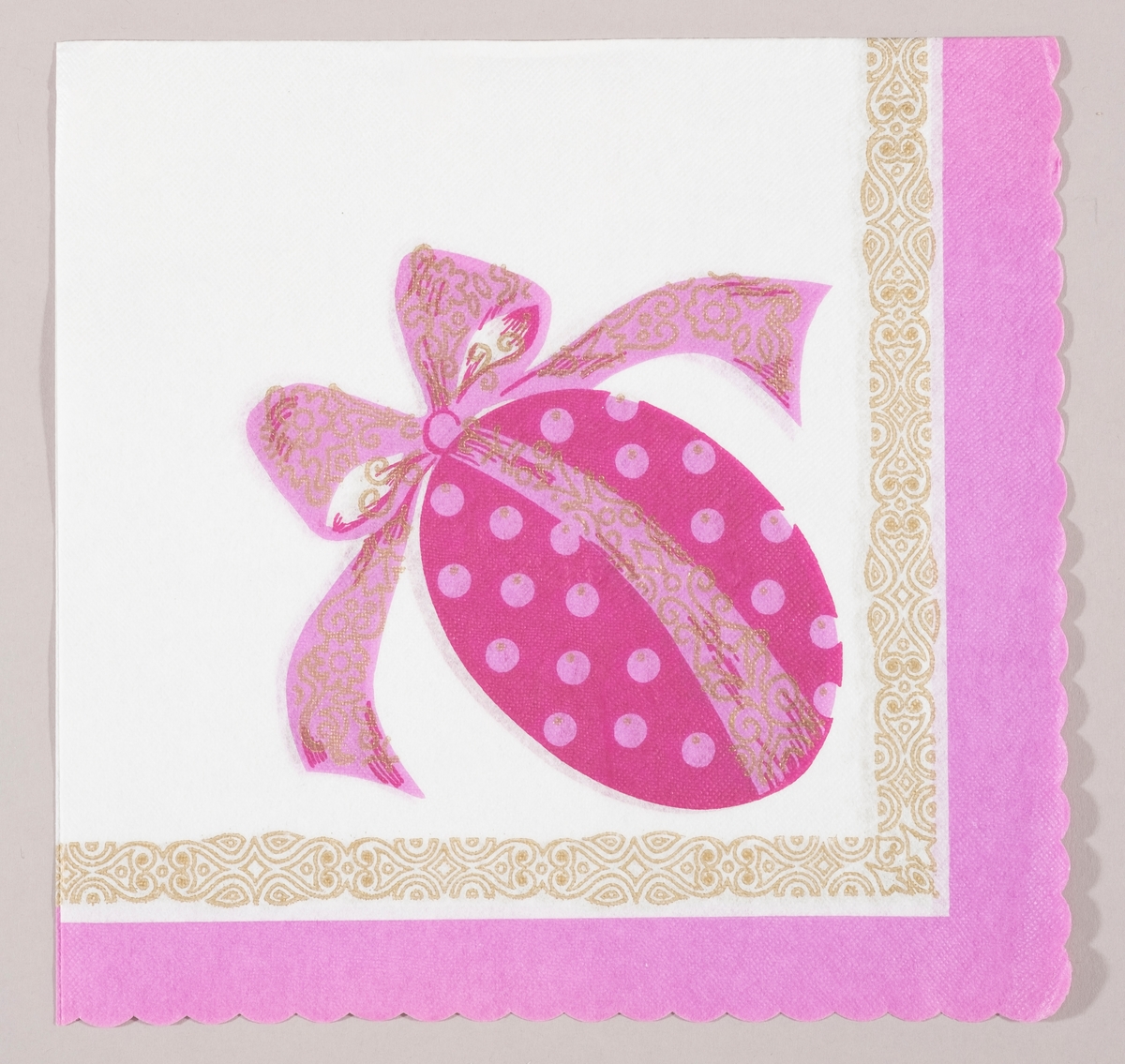 Et lilla påskeegg med rosa prikker og en stor rosa sløyfe med gullmønster. En mønstret bord i gull og lilla kant.