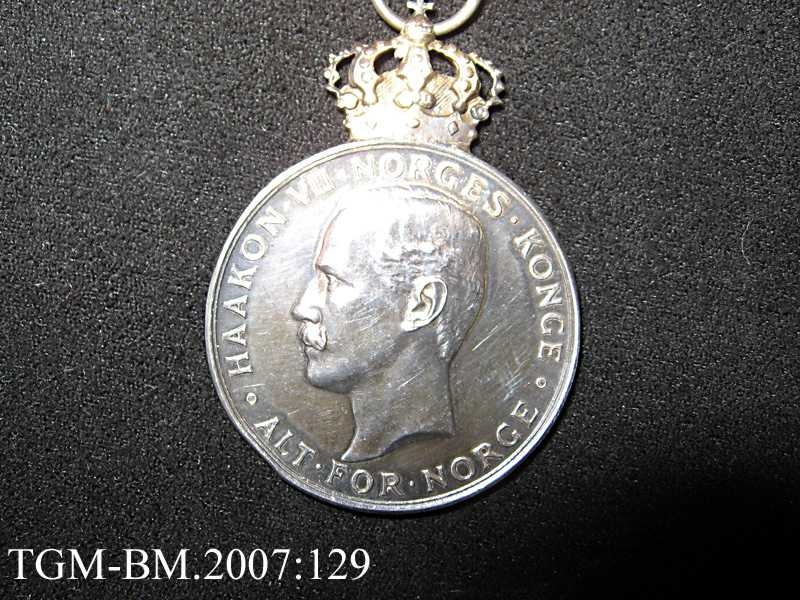 Medaljen ligger i en liten, flat, burgunderrød eske (original-etui) - preget med en forgylt krone på lokket. Silke og fløyel innvendig.