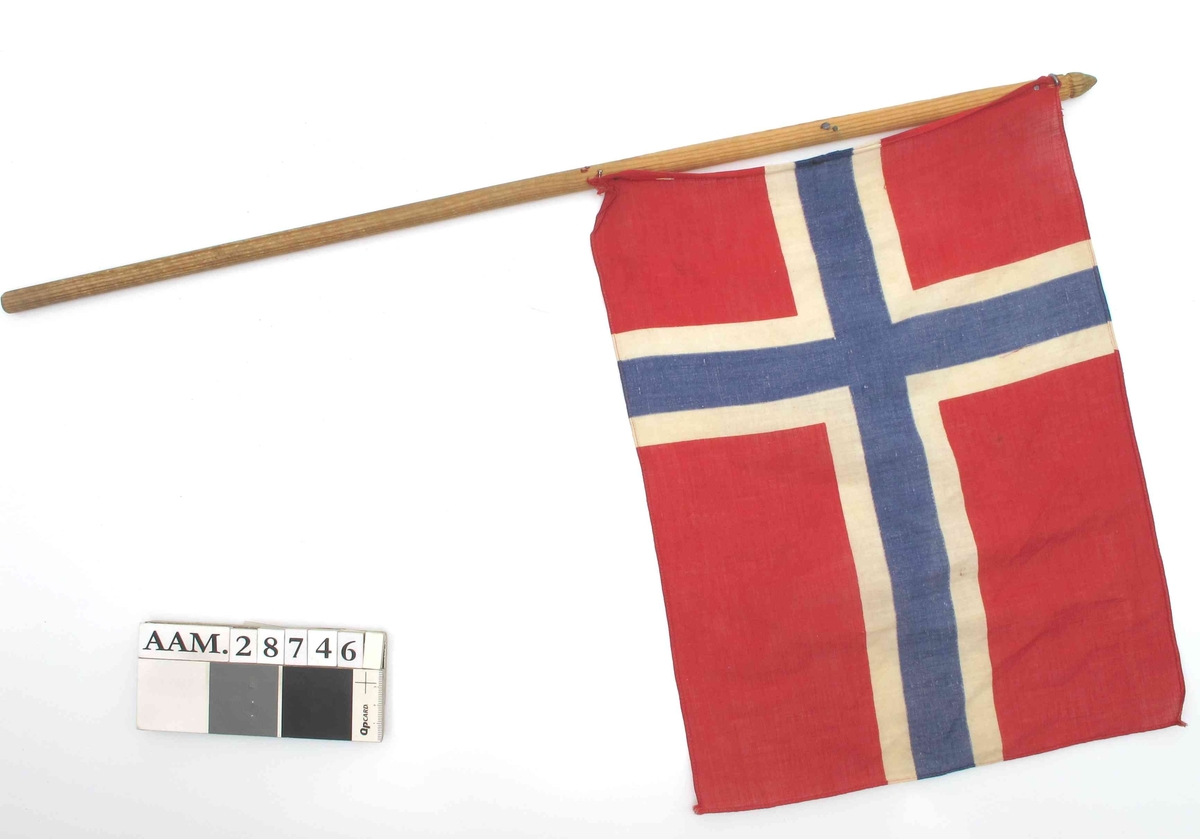 Trestang med påstiftet trykt norsk flagg. Stiftingen er fornyet, men dårlig utført.