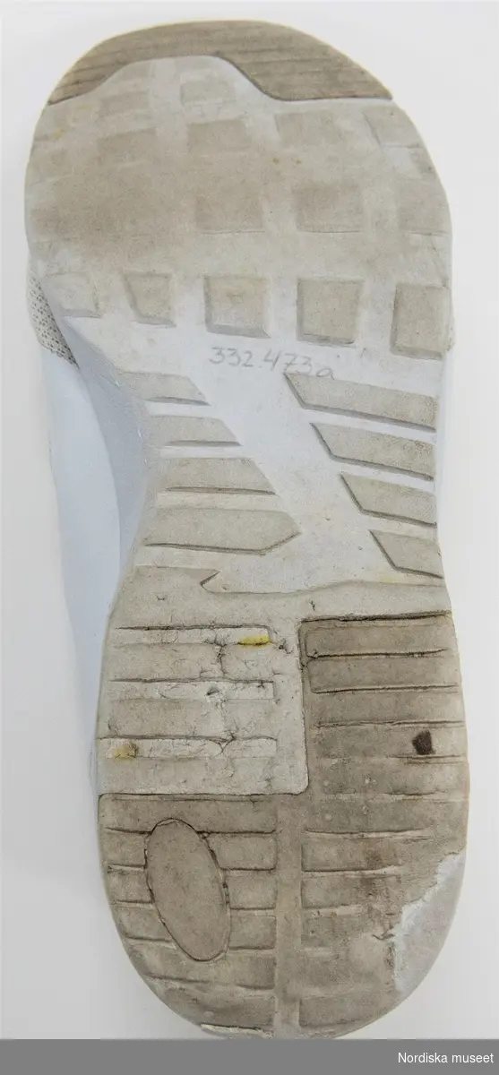 Ett par vita sneakers. Sula av plast (phylon och TPR=ThermoPlastic Rubber) med transparent plastbit under i hälen. Överdel av syntettyg och läderimitation. Snörning med vita platta skosnören genom sju par hål. Plös. Insida av syntettyg. Liten bandögla på bakkappan. 
På plösen etikett med text: 
"157 SOULS
STYLE: O2/A Shoe
SIZE: EU 45
SIZE: EU 11
MADE IN CHINA"
På innersulan svart text: "...157 SOULS".

Anmärkning: text delvis bortnött på innersulan. Bruna fläckar på ovansidans främre del.
/Leif Wallin 2017-06-07