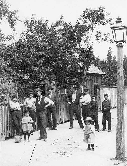 Fabrikör A E Bolling utanför sitt gjuteri på Bergsgatan med arbetare, och några barn. Bolling har ljus hatt med mörkt band och väst. Till höger en av de gamla gatlyktor som var i bruk 1848-1905.