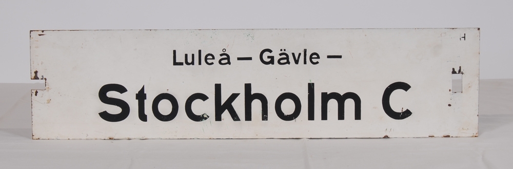 Destinationsskylt av plåt med viitmålad botten och svart schablonmålad text. På ena sidan står det: Luleå-Gävle-Stockholm C, på andra sidan: Stockholm C-Gävle-Luleå. Slutdestinationen står med större text. I ena ändan av skylten finns ett rektangulärt jack och i andra änden ett rektangulärt hål.