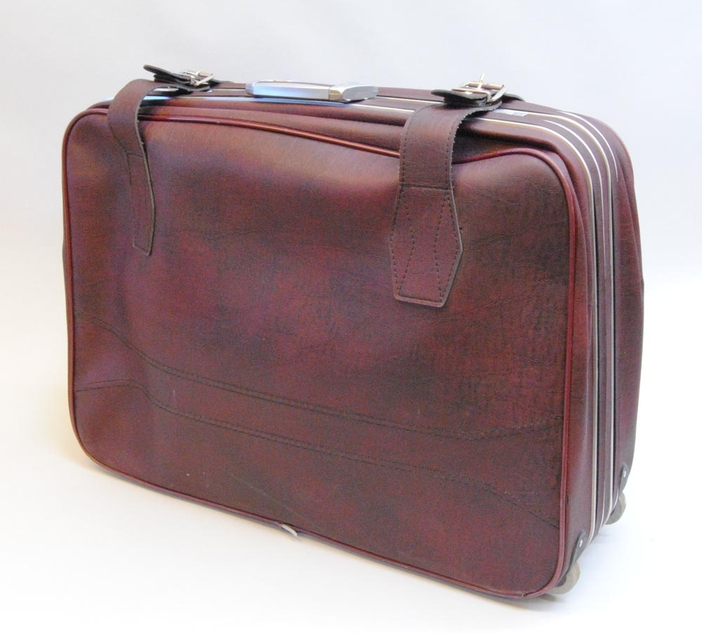Resväska av rödbrun galon med hjul. På väskan sitter en skylt med texten "alstermo". Hjulen sitter på ena kortsidan och motstående sida har ett utdragbart handtag att dra väskan i. Väskan är försedd med spännband och lås.
Inuti är väskan inredd i ljusgrå matt textil med fickor och spännband. Inuti väskan finns ett mellanlägg (:2), nyckel (:3) och en skopåse (:4).