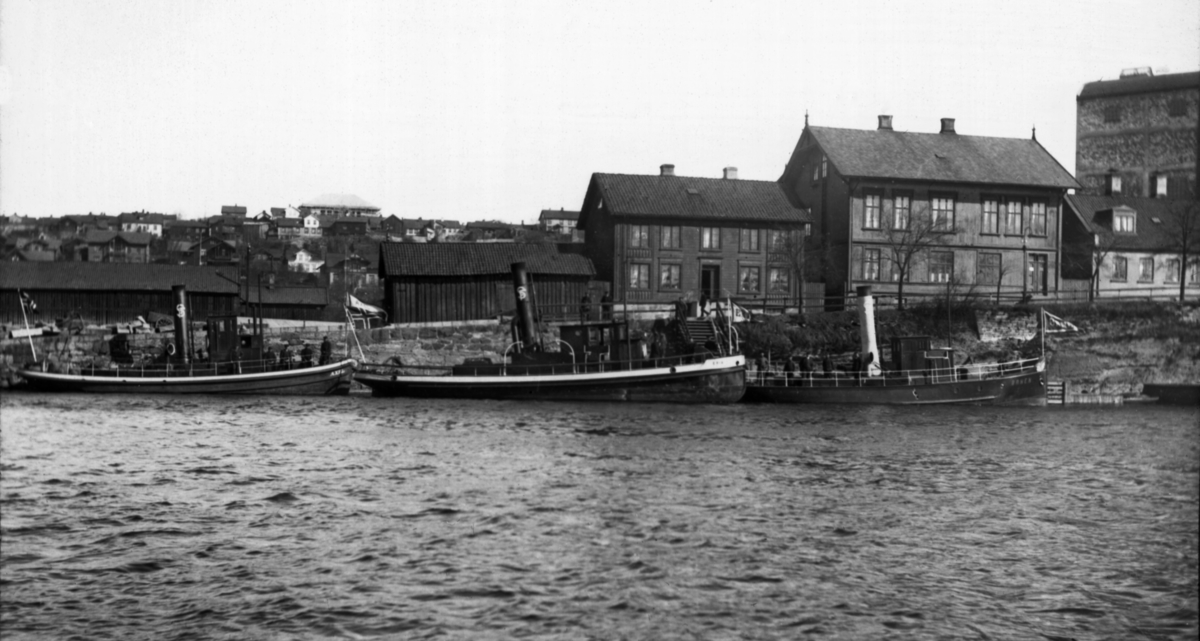 Skiensvassdragets Fellesfløtningsforenings slepebåter D/S Axel, D/S Erik og D/S Ørnen fotografert foran kanalkontoret i Skien i 1911.  D/S Axel ble innkjøpt fra Wilhelmsbergs mekaniska Verkstad i Göteborg i 1903.  Den fikk navn etter fløtningsforeningens administrative leder, Axel Borchgrevink.  Båten hadde opprinnelig en 80 hestekrefters dampmaskin, som ble erstattet av en dieselmotor i 1954.  Slepebåten Axel gikk som tømmersleper for Skiensvassdragets Fellesfløtningsforening helt fram til 1999.  Den trafikkerte hovedsakelig Vestvatna (Bandak, Kviteseidvatnet og Flåvatn).  D/S Erik ble bygd ved Porgrunds mekaniske Værksted i 1901.  Båten ble oppkalt etter trelasthandler Erik Rasmussen fra Porsgrunn, som hadde vært medlem av styret eller direksjonen for Skiensvassdragets Fellesfløtningsforening i perioden 1883-1901.  Her investerte organisasjonen i en 150 hestekrefters vinterstid.  Båten ble ombygd fra damp- til dieseldrift i 1952.  Den var i drift som fløtingsbåt fram til andre halvdel av 1980-åra.  Skiensvassdragets Fellesfløtning kjøpte D/S Ørnen i 1905.  Den var bygd ved Ørens mekaniske Verksted i Trondheim for konsul Iver Huitfeldt.  Den hadde, som D/S Axel, 80 hestekrefters dampmaskin.  D/S Ørnen gikk i hovedsak på strekningen mellom Løveid og Porsgrunn.  Den ble ombygd til dieseldrift i 1951.  Den var i drift som tømmerslepebåt fram til midten av 1960-åra. Kanalkontoret i bakgrunnen huset administrasjonen for Telemarkskanalen og administrasjonen for Skiensvassdragets Fellesfløtningsforening fram til 1902.  Da, etter Axel Borchgrevinks død, fikk de to organisasjonene hver sine ledere, og Fellesfløtningsforeningen flyttet til egne lokaler, i første omgang i en bygning brukseier og konsul Thorvald Schiøtt eide på Broene i Skien, seinere i Nedre Hjellegate. 