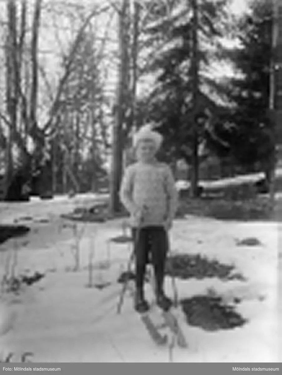 En pojke står på ett par skidor i en skog, troligtvis 1920-30-tal. På marken ligger snö. Det är samma gosse som 2018_0100.