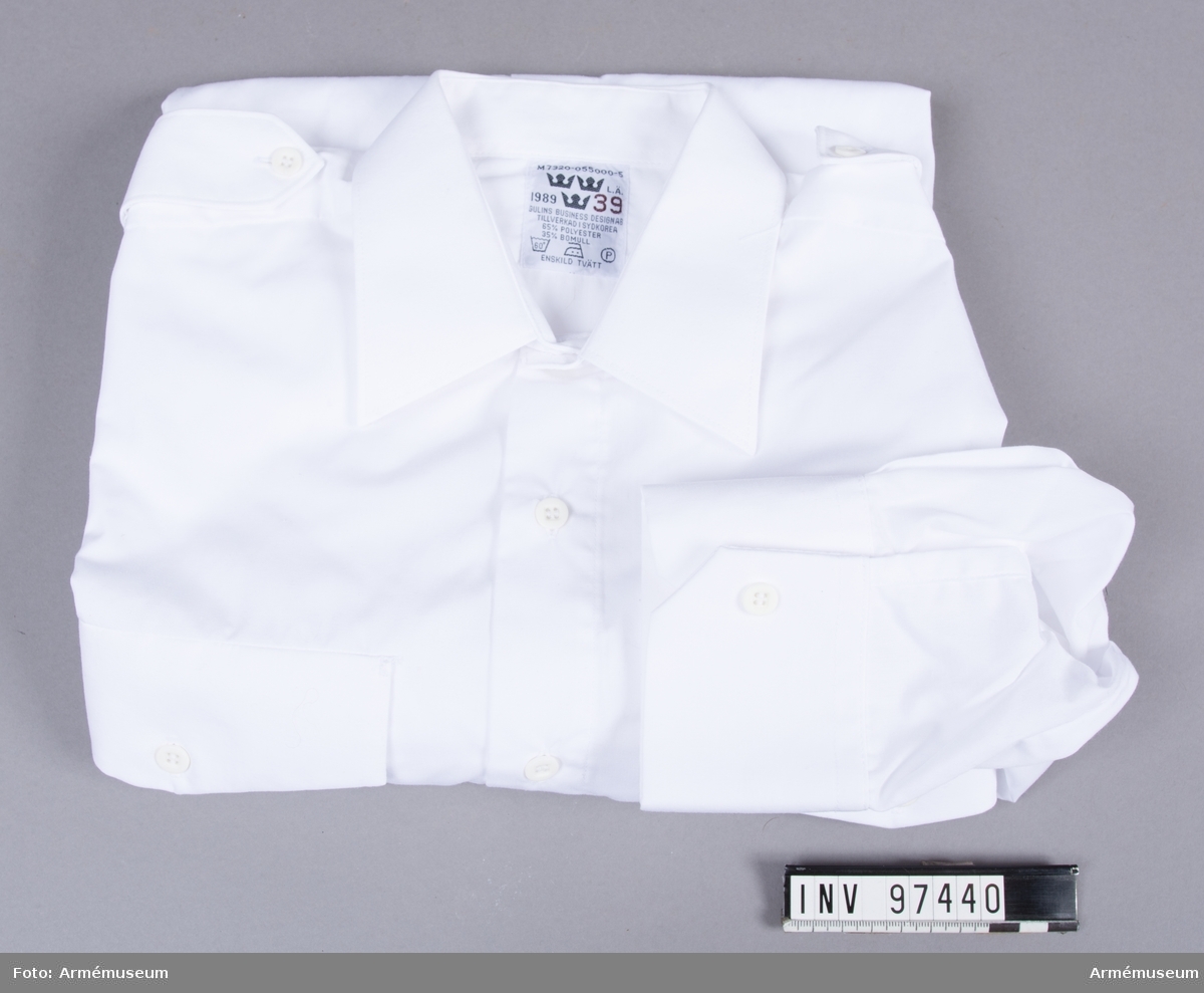 Vit skjorta i polyester och bomull, tillverkad i Sydkorea 1989. Med axelklaffar där axelhylsor kan fästas.
