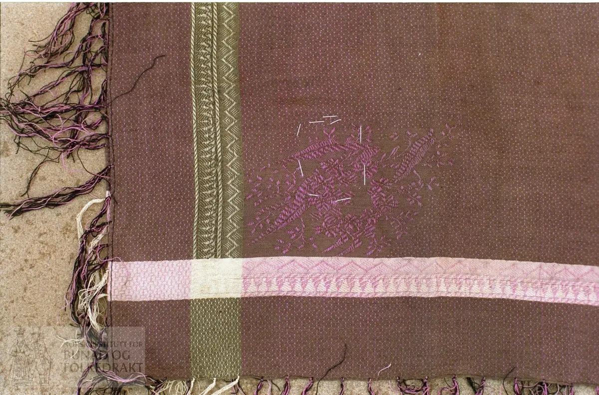 Blandingskvalitet, rosa, brungrått og grønt med rosa brokaderoser.  Påsatte silkefrynser i rosa og svart.  Maskinfald rundt.  72  x  73 cm.