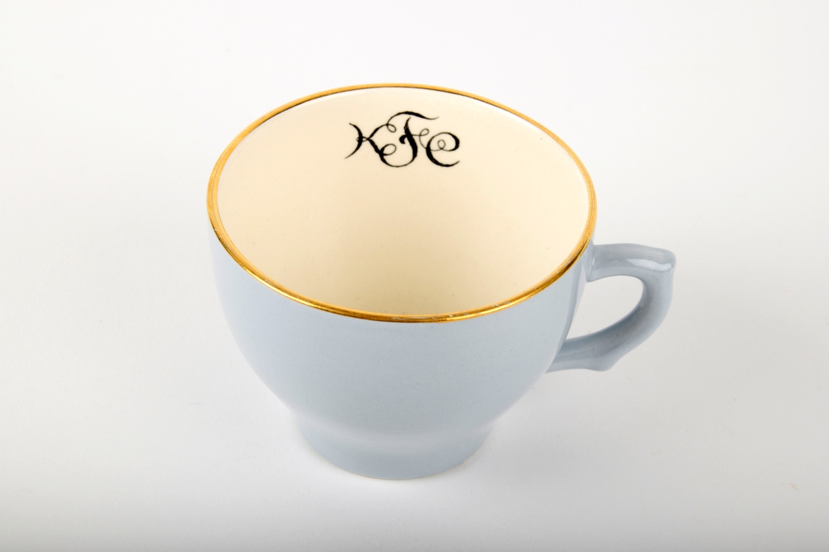Kaffekopp med fat. 

Koppen har monogram på innsiden. Både koppen og fatet har gullfarget kant. Fatet er hvitt i midten.