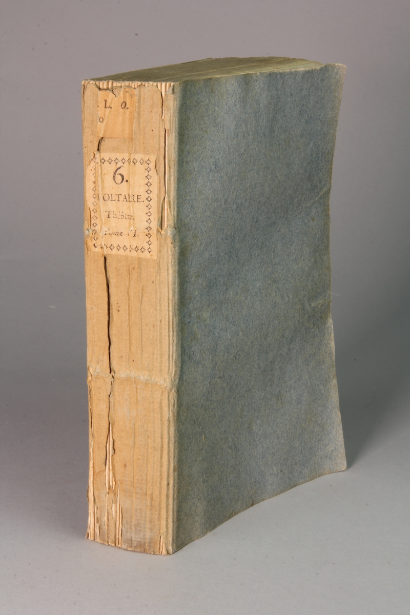 Bok, häftad,"Oeuvres complètes de Voltaire." del 6, tryckt 1785.
Pärm av gråblått papper, skurna snitt. På ryggen pappersetikett med tryckt text med volymens namn och nummer. Ryggen blekt.
