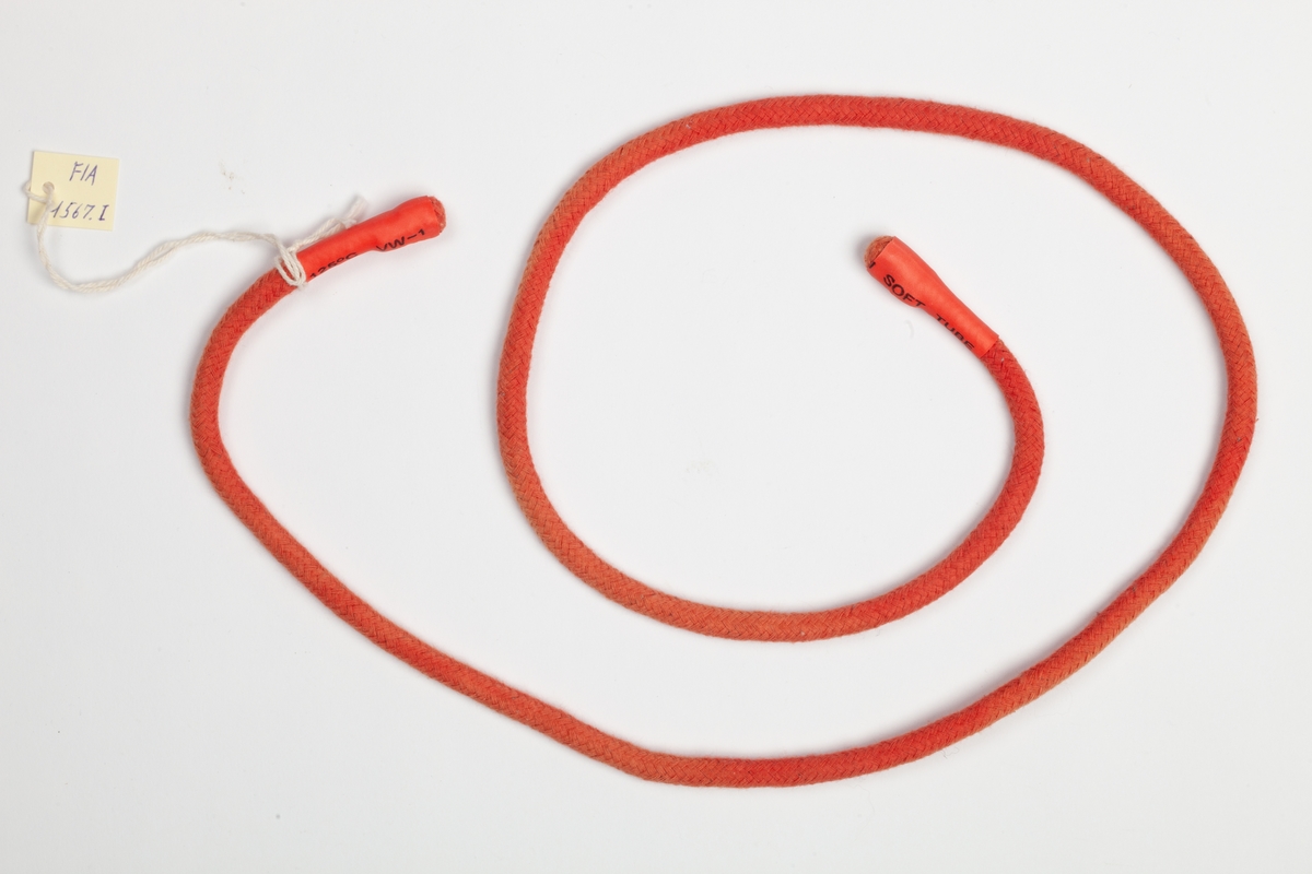 En rundvevet rød smal rem med gummiender. Turnikèen kan snøres sammen om et lem ved livstruende skade eller huggormbit.