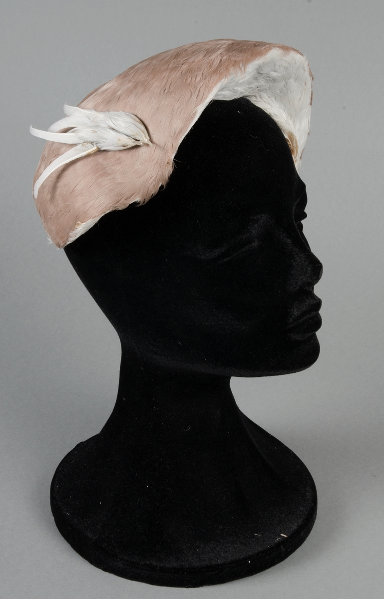 Hatt tillverkad av lilafärgade dun klädd på stramaljliknande material. Invändigt sidentyg. Liten stålfjäder fäster huvudprydnaden vid huvudet. Gummisnodd under hakan.
