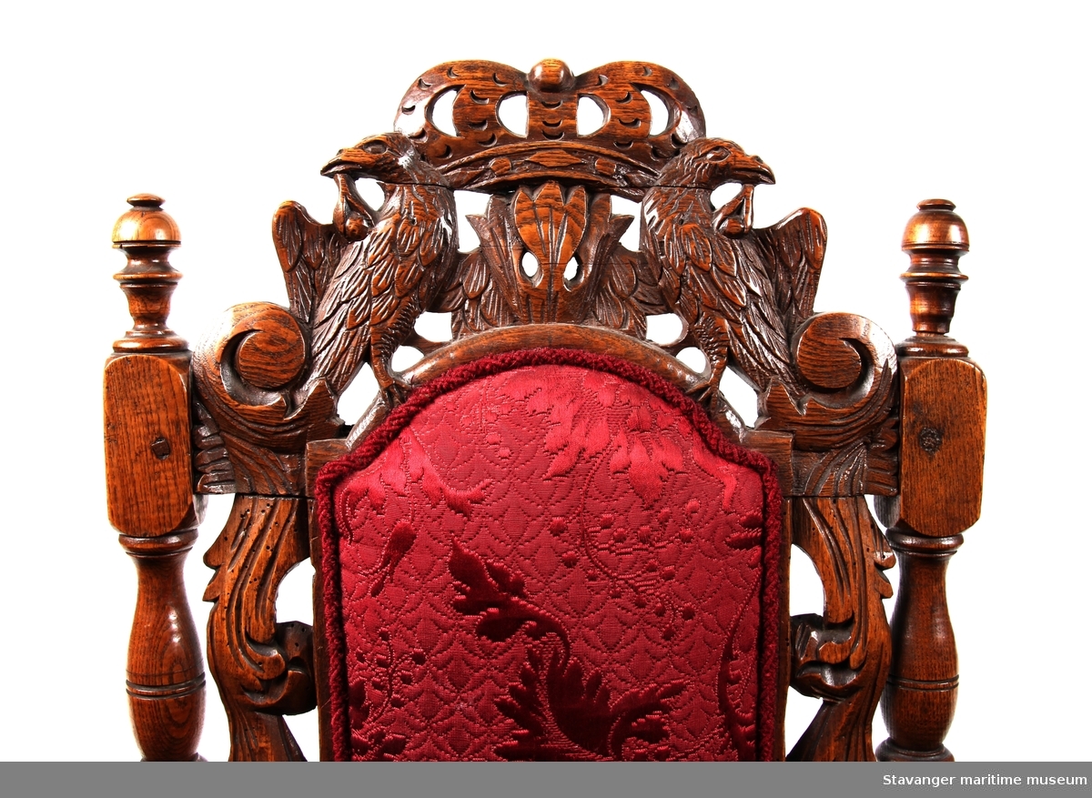 Høyrygget barokkstol av eik med rødt brokadetrekk. Rygg såvel som forben med tilhørende brett er utskåret med dyr og akantusranker.

Sekundært trekk. Ryggen er forsterket  på baksiden i nedrekant.