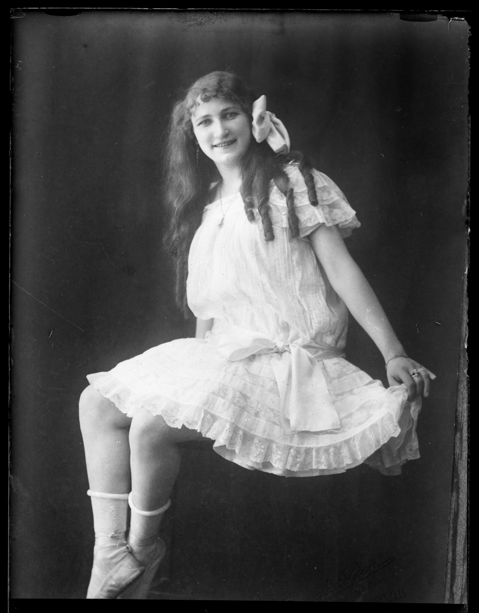 Rosa Wrobello i vit knälång klänning, vita strumpor och vit rosett i håret.