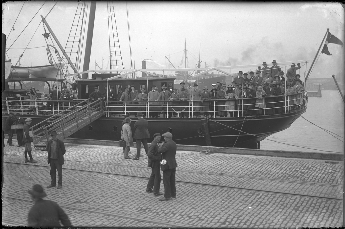 Ett passagerarfartyg ligger inne i hamnen och görs redo för avfärd. Ett antal passagerare står på däck och på kajen står också människor. I fotografens egna anteckningar står: Danmarksresan, Fiona i Göteborgs hamn.