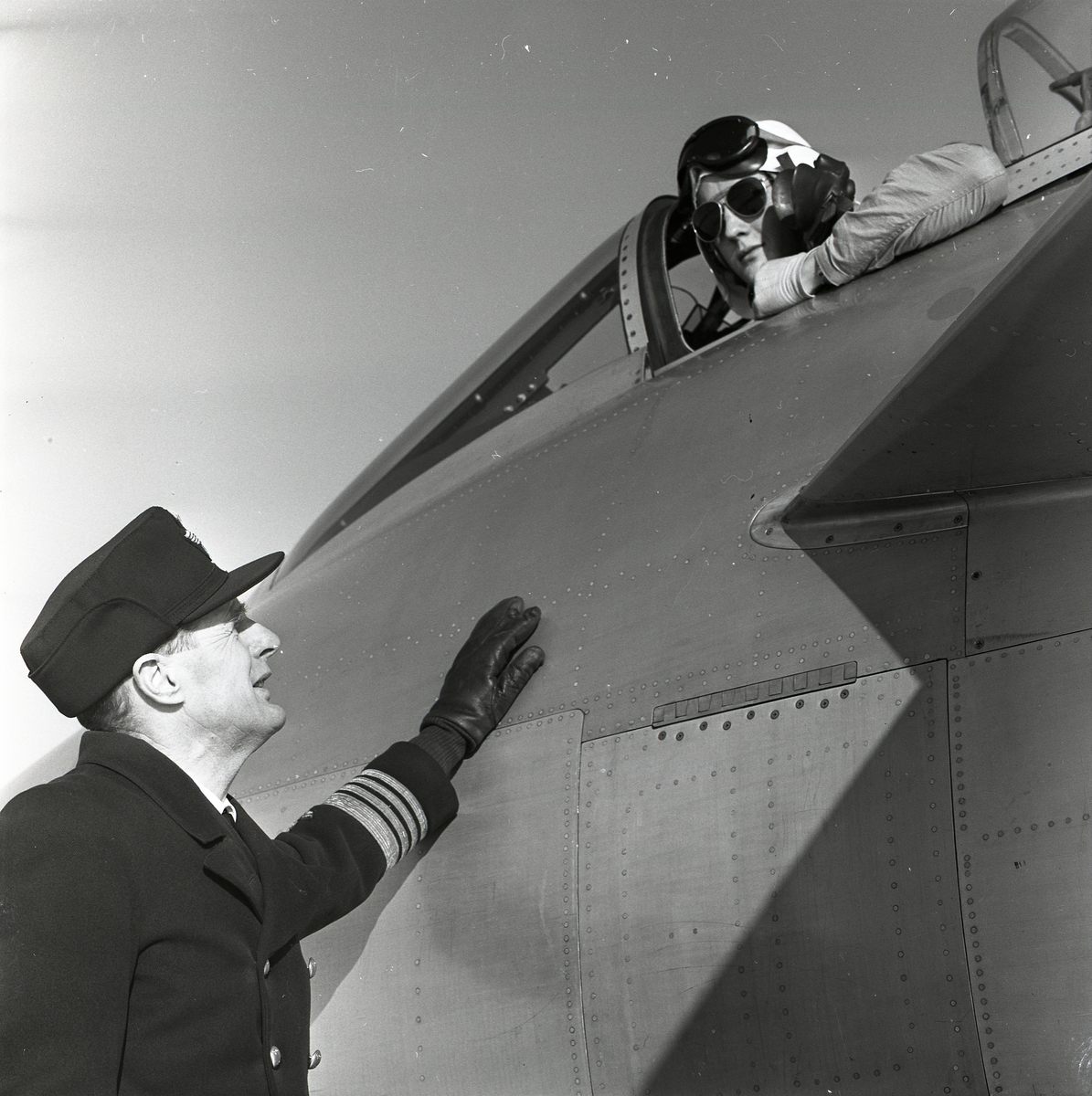En man i militäruniform står nedanför ett flygplans förarkabin och ser upp mot piloten den 31 januari 1957.