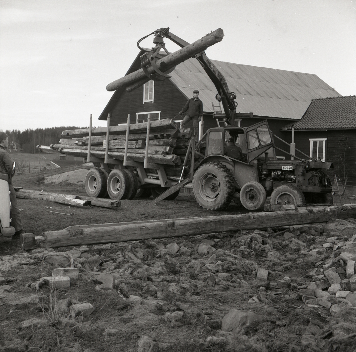 En man lastar timmerstockar med sin traktor på en vagn i Rengsjö, 1967.