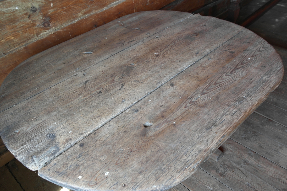 Bord i hugget, høvlet og pusset furu. Bordet har oval bordplate som er satt sammen av tre bord, samt  bukkebein som er avstivet på langs med to brede bord.
