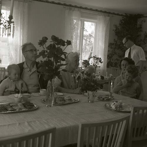 Några människor, både barn och vuxna, sitter vid ett fikabord, 1968.