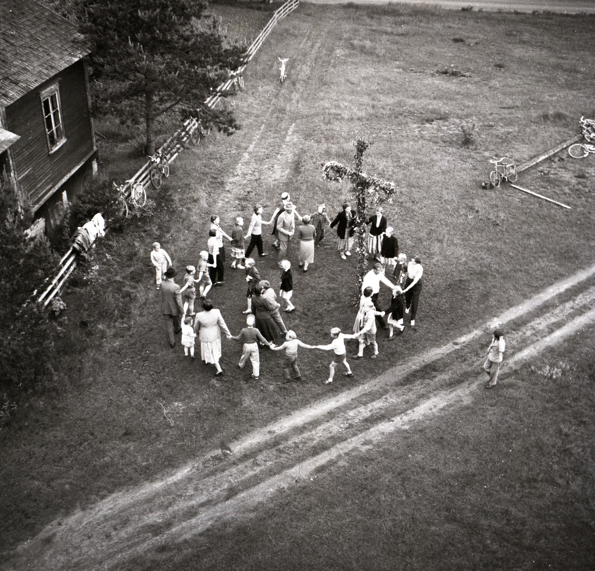 En grupp människor dansar runt en midsommarstång i Glössbo, 25 juni 1954.