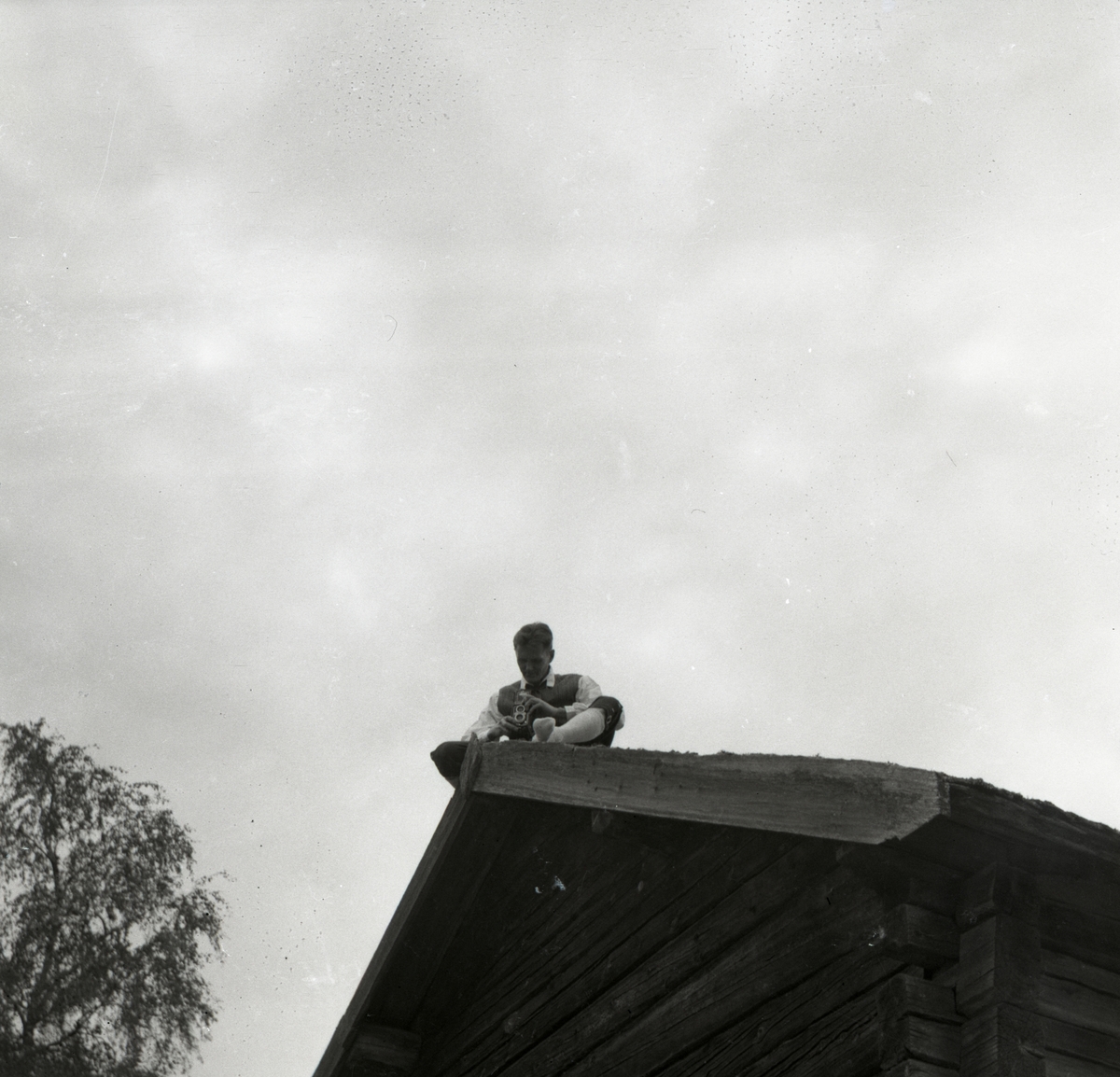 Hilding Mickelsson sitter på ett tak vid Rengsjö hembygdsgård och fotograferar, 9 september 1956.