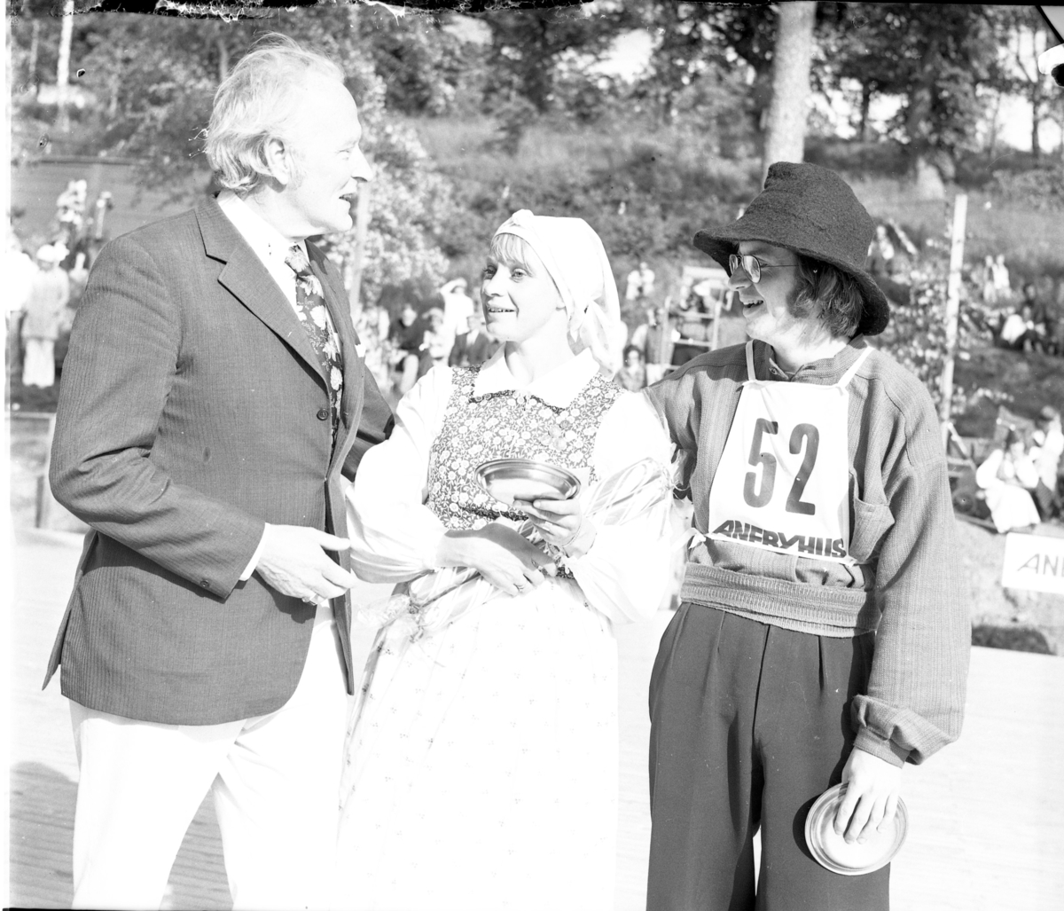 Grännapolkan på Grännaberget, 1975. Danspar nr 52, troligen segrarna Gunnel Johansson och Ola Holmberg från Uppsala intill man som troligen är prisutdelare. Dansparet har tennfat och stor polkagris i famnen.