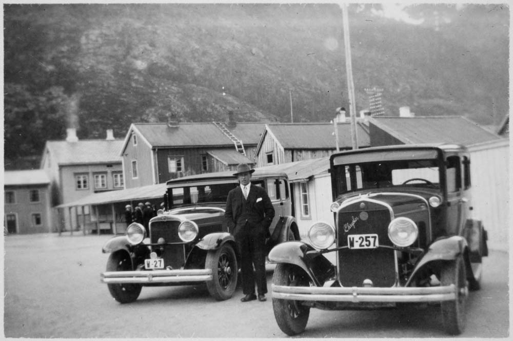 Drosjesjåfør Gunnar Wikborg Vik på drosjeholdeplassen ved fisketorget i Mosjøen mellom en Nash 1930 og en Chrysler 1930.