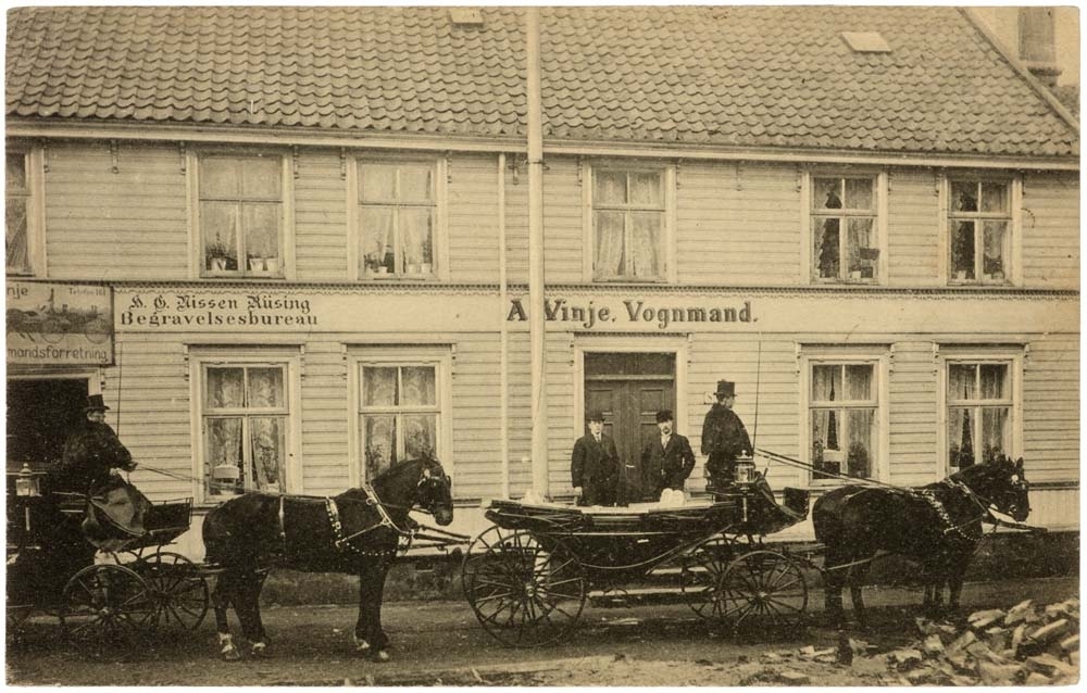 Postkort av hester og vogner utenfor A. Vinje Vognmand og H. G. Nissen Rüsing Begravelsesbureau.