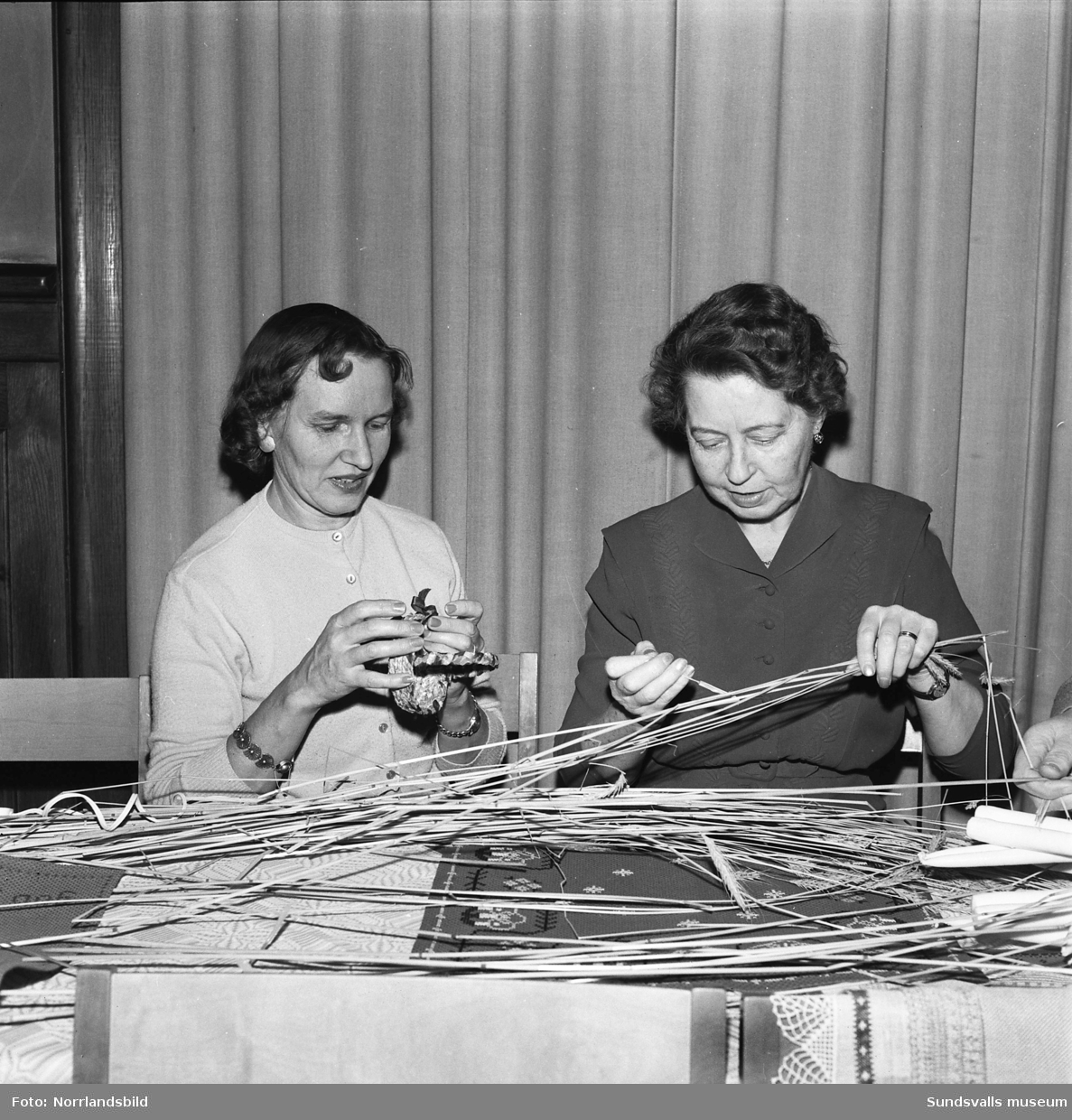 Två kvinnor tillverkar julprydnader av halm för försäljning på julmarknad.