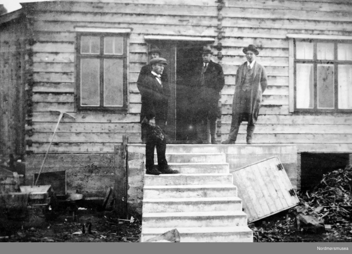 Foto av fire menn på trappen til et bolighus. Et bilde fra en samling fotografier med bureisingsfelt i Norge. Originalmaterialet tilhører Norsk myrmuseum i Smøla kommune. Fra Nordmøre museums fotosamlinger.