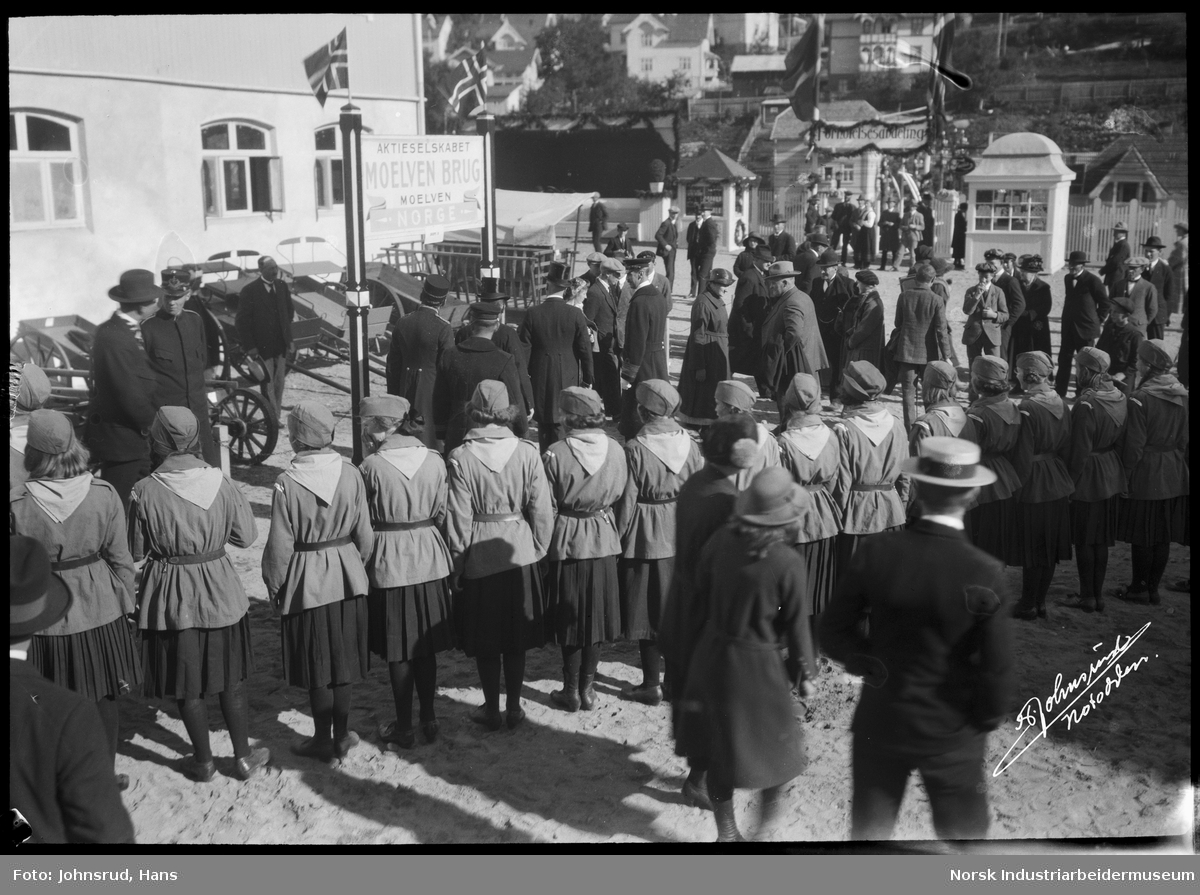 Åpning av Fylkesutstillingen 1922 med besøk av Kong Haakon VII. HM Kongen går langs veien, jenter i uniform oppstilt.