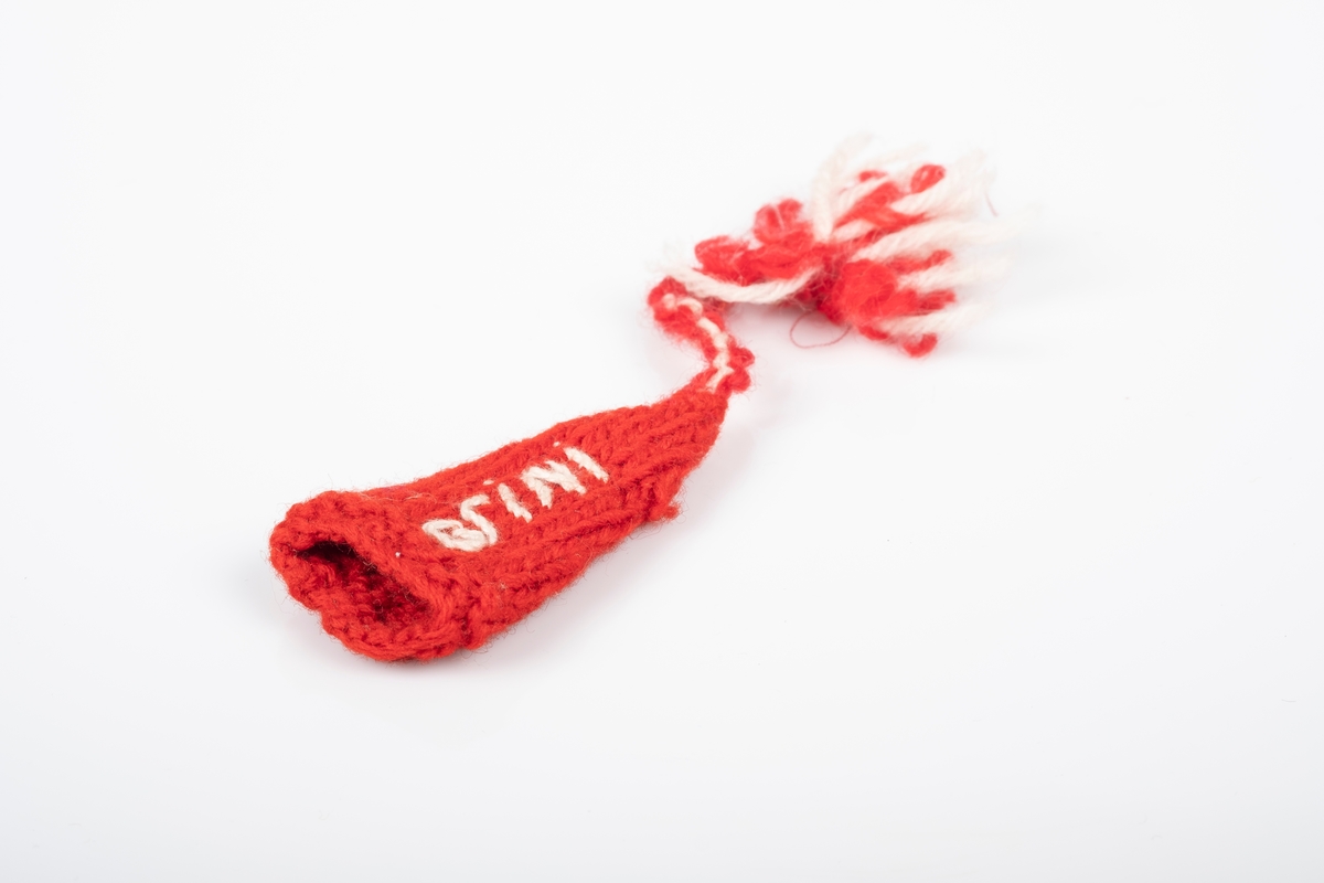 En liten rød strikket lue med en rød og hvit dusk. Det er brodert "Grini" på luen. Luen ligner en nisselue.