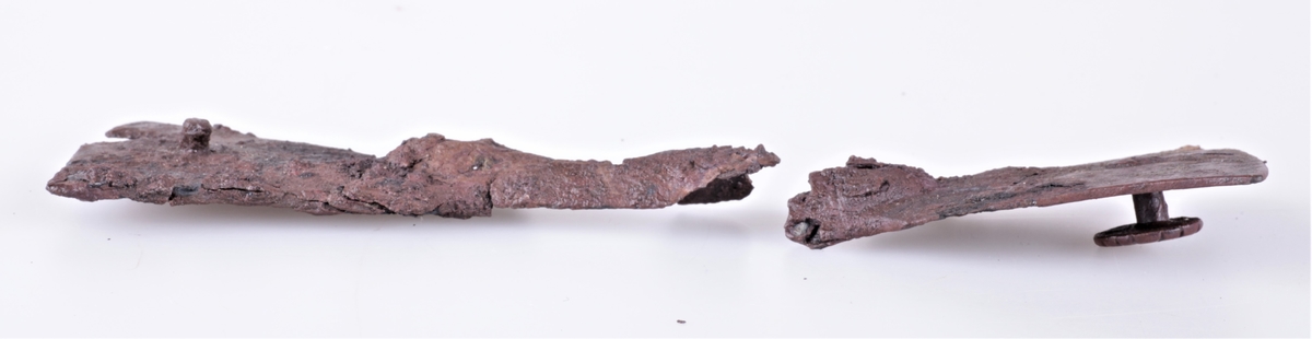 Skjoldhåndtakbeslag i jern fra folkevandringstiden funnet i gravhaug ved Gjerstad gård i 1882. Håndtakbeslag av jern i 2 deler, nærmest R 222 (a og b). a) bredde i enden 6 cm, b) bredde i enden 6 cm. c) et krummet, flatt beslagstykke av jern, lengde 7,5 cm.