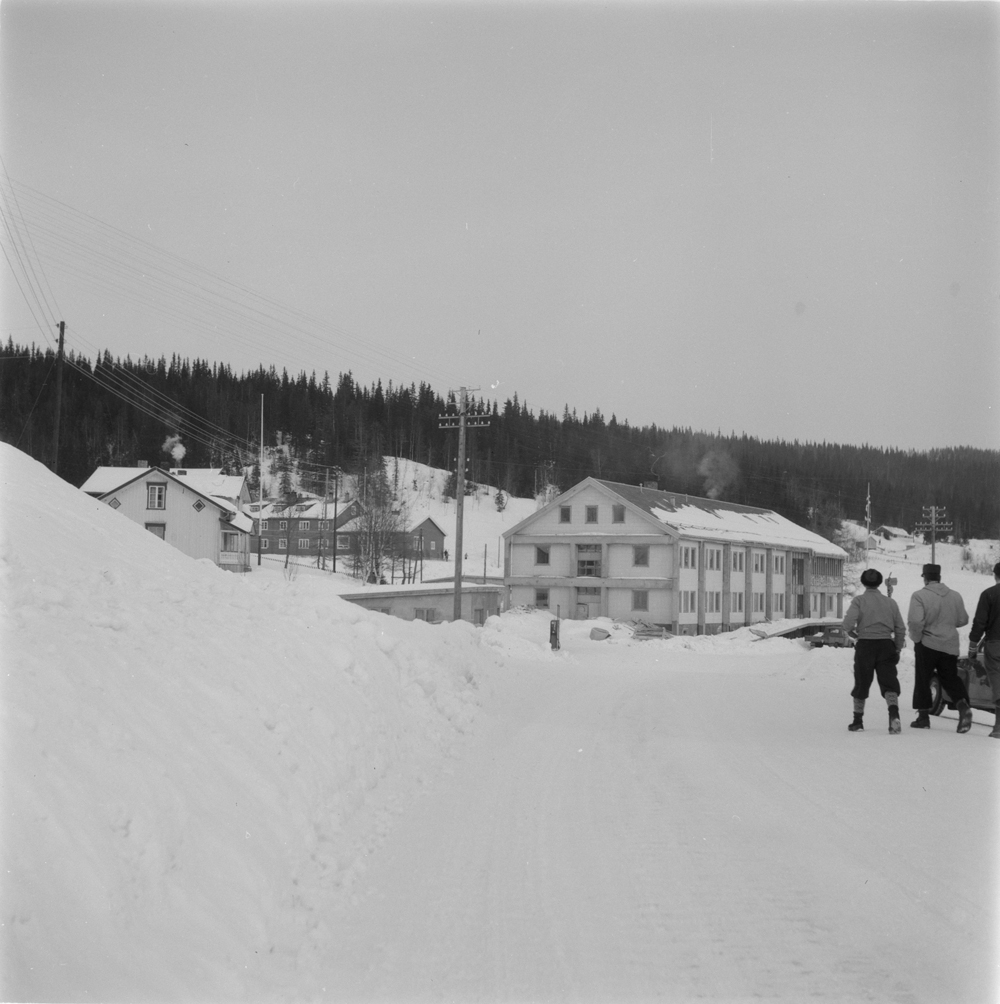 Herredshuset i Hattfjelldal. Vinter, personer som går på veien, noe av bebyggelsen ved siden av.