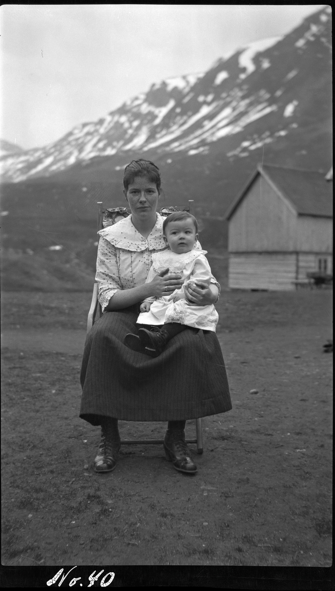 Portrett av sittende kvinne med barn, tatt utendørs med fjell i bakgrunnen.
