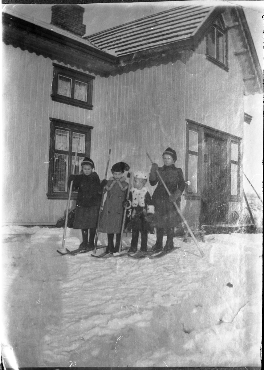 Avfotografert bilde av fire uidentifiserte barn på ski foran et våningshus.