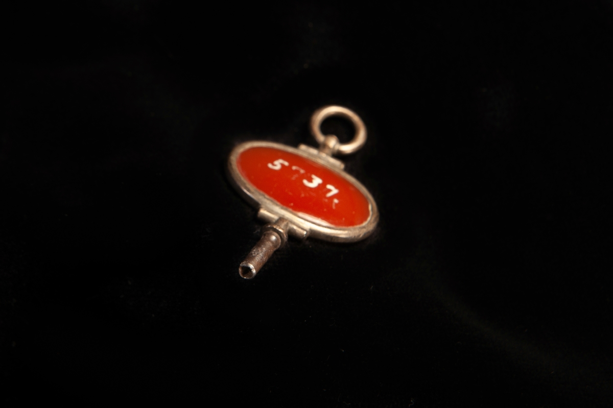 En urrnyckel av silver med en roströd karneolsten i handtaget. Två otydliga stämplar på ringen.