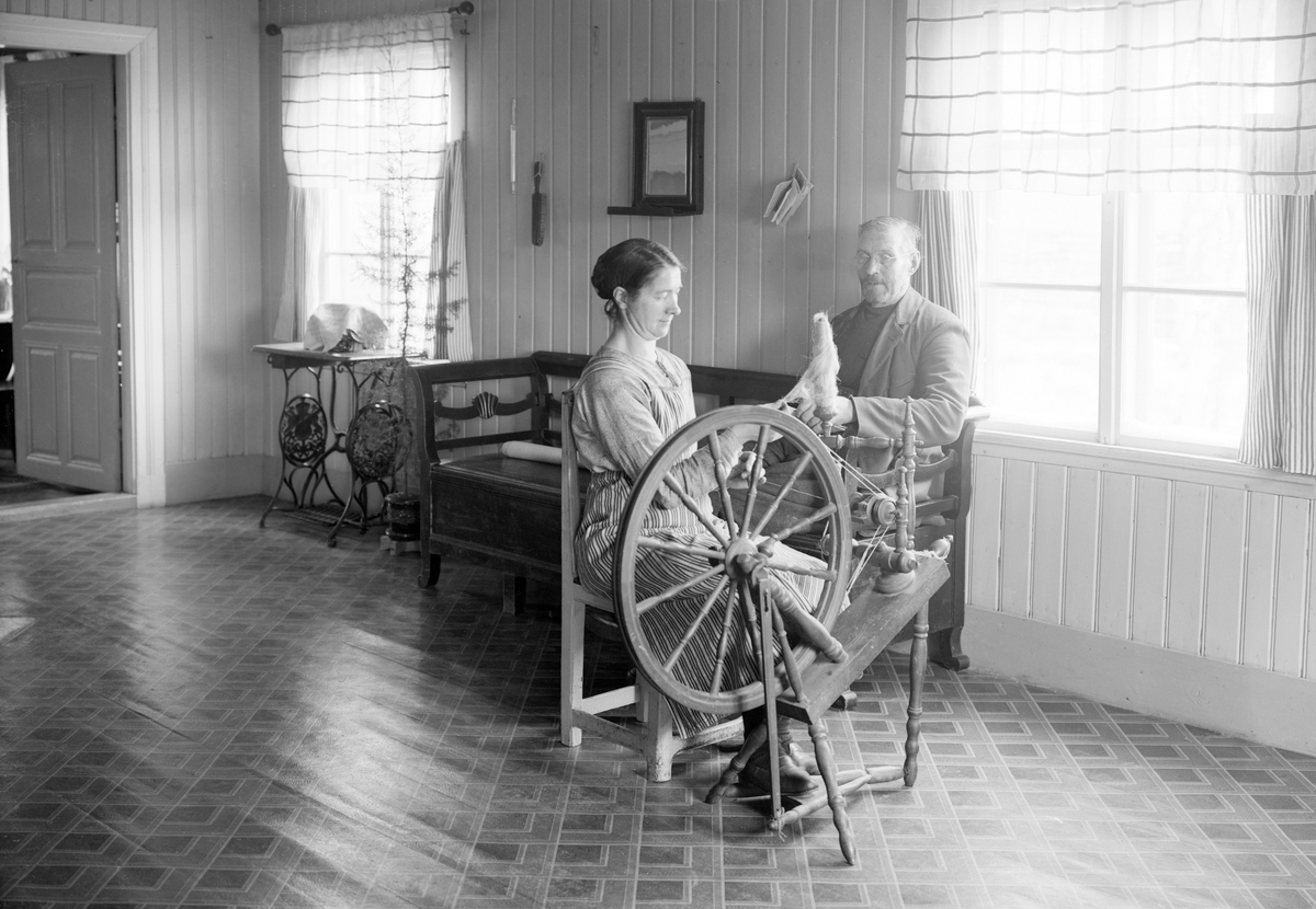 Nämndman Per Johan Pettersson och hans hushållerska Sofia Axelsson har tagit plats vid fönstrets ljus för läsning och spånad. Fotografiet dateras varligt till omkring 1925-30.