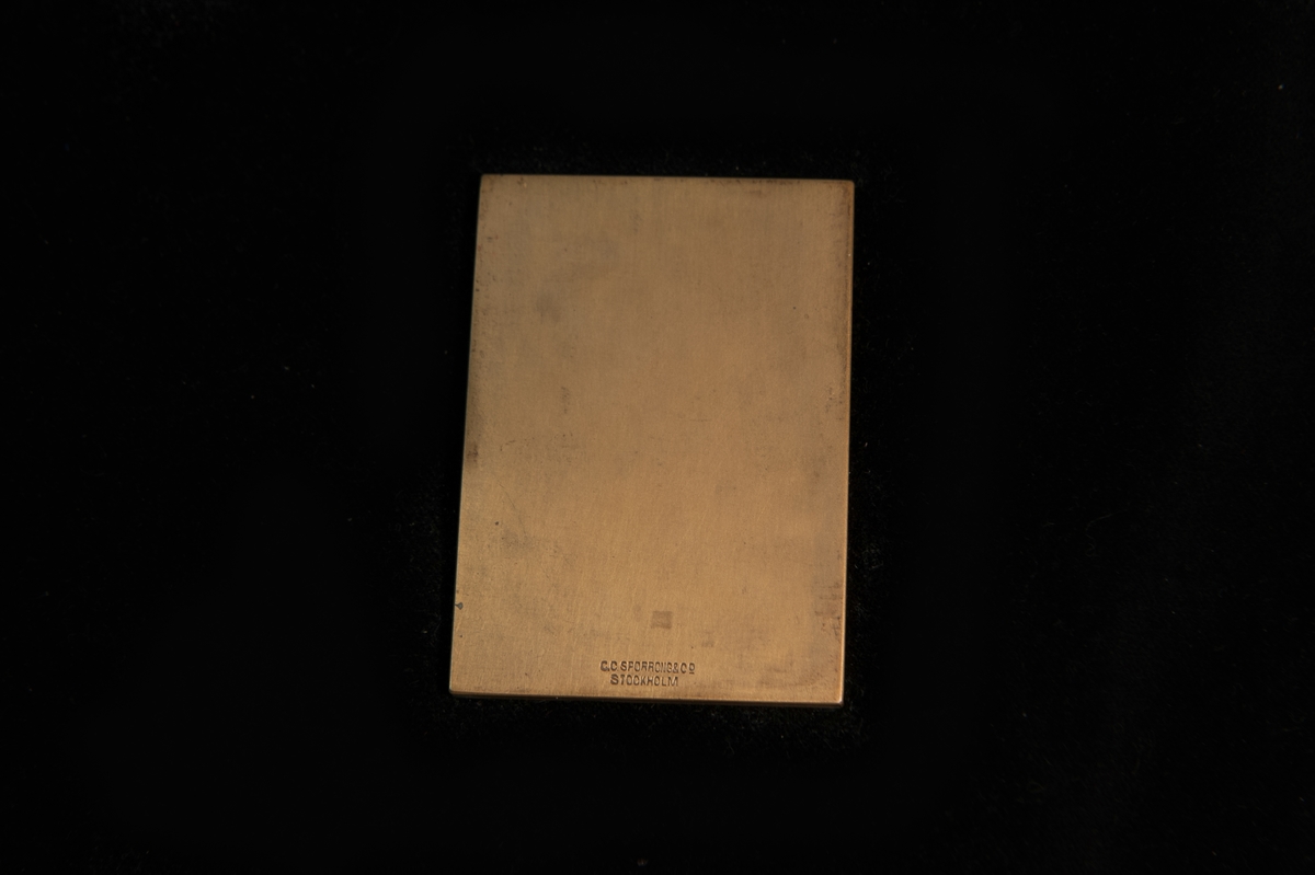 Plakett i brons i mörkblå pappask med gulddekor. Åtsida: Husqvarna Vapenfabrik (1689-1939) från ovan. Med anledning av Husqvarnabolags 250-årsjubileum. Frånsida: (tom). Plaketten är tillverkad av C.C Sporrong & CO