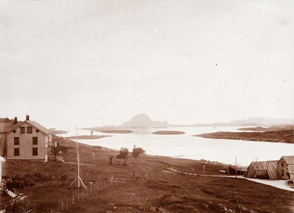 Torghatten sett fra Masterberget i Brønnøysund. Telegrafekspedisjon, naust, båt, bygninger. To barn midt på bildet. Til høyre sees Biskopholmen, til venstre ligger Tauterskjæret.