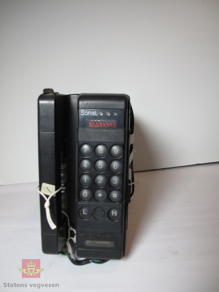 Bærbar, svart mobiltelefon. Rektangulær kasse, med telefonrøret på toppen og batteriet i bunnen. Telefonnummeret til telefonen var 094-54085. Batteriet er tatt ut og er av typen 2x6 V. 5,6 Ah.