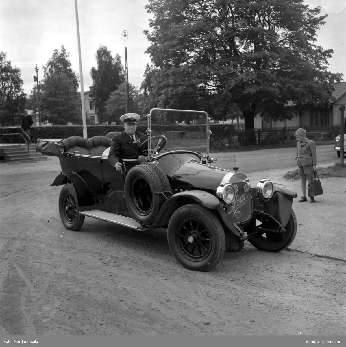 Gamla veteranbilar på planen invid Västra station, Åkersvik. Bland annat Fritiof Larsson med sin Horch invid en liten Fiat 500 med registreringsnummer Y42B, två unga kvinnor tittar upp genom bilens taklucka. På tredje bilden en Ford från 1908, i bakgrunden Kronohäktet.