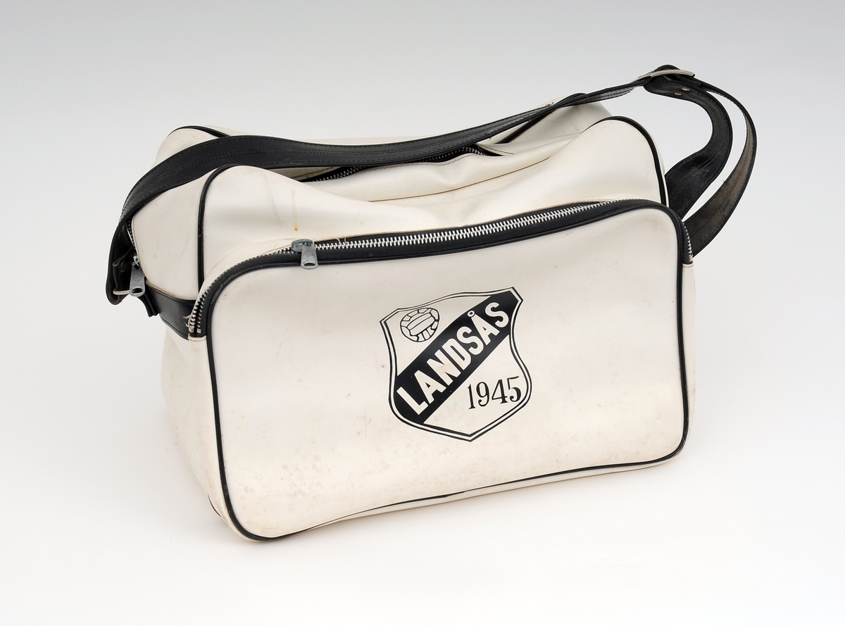 Hvit sportsbag framstil av skai med svart regulerbar skulderstropp. Vesken har to rom som kan lukkes med glidelås. Logoen til Landsås Fotballklubb i sort på den ene siden.