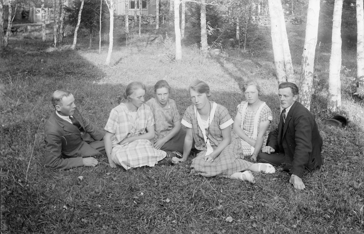 Unga kvinnor och män sittandes i trädgård, Alunda, Uppland