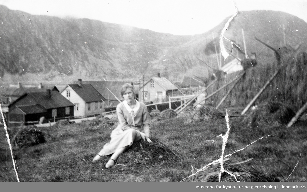 Nordvågen. Astrid Helgesen foran høyhesjer. I bakgrunnen bebyggelse. Ca. 1928/29.