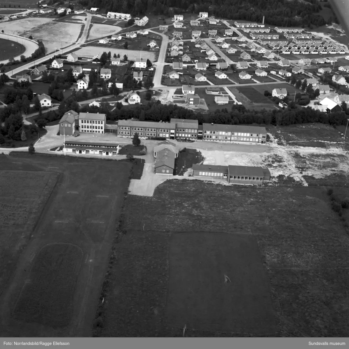 Flygfoto över Bergsåkers centralskola taget söderifrån. Norr om skolan villaområde och i vänsterkant skymtar travbanan.